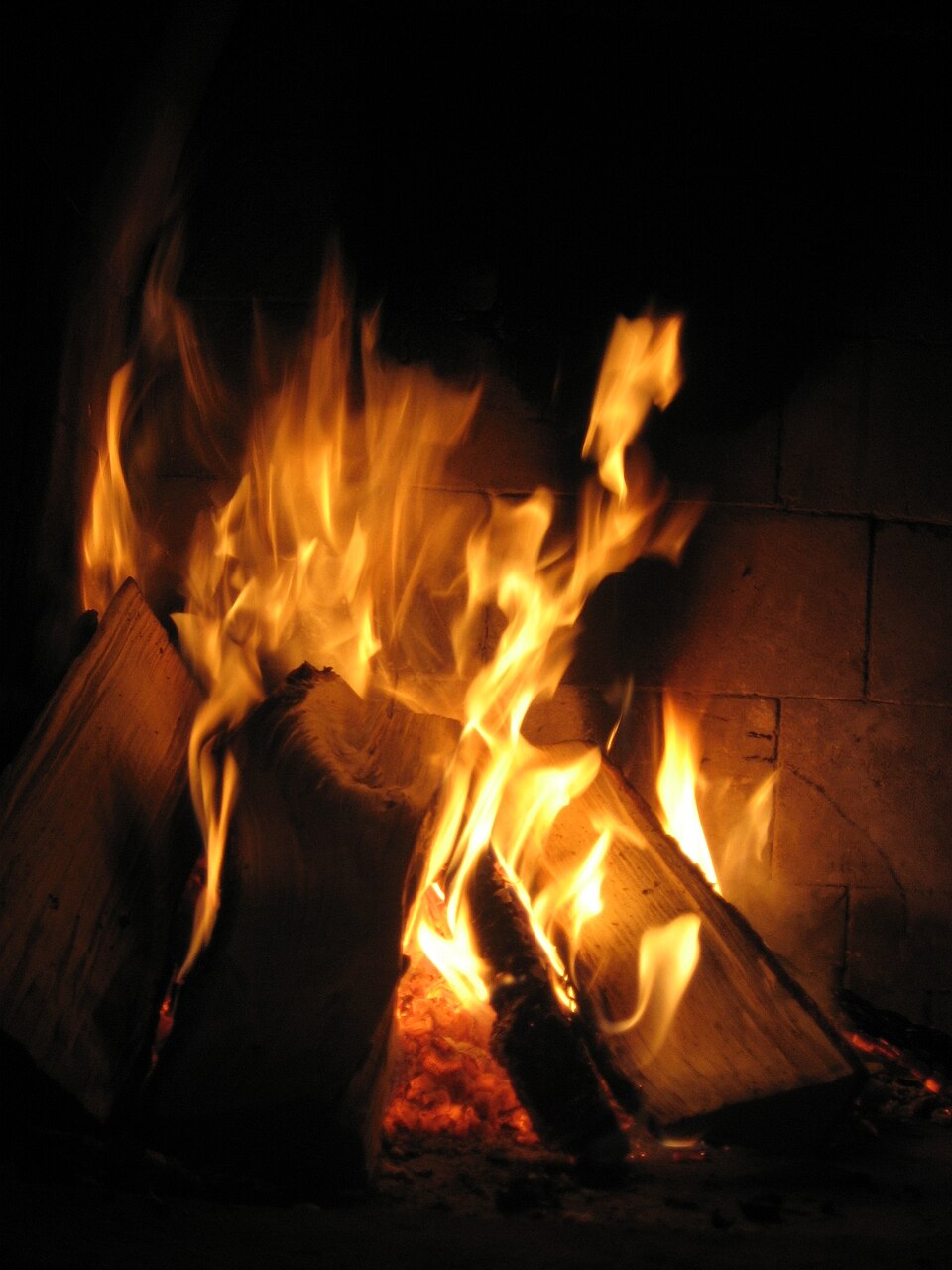 Feu de bois allumé dans une cheminée, avec des bûches disposées en pyramide et des flammes vives.